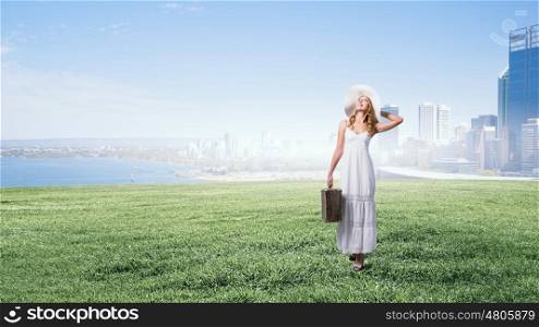She is traveling light. Woman with suitcase in white long dress and hat