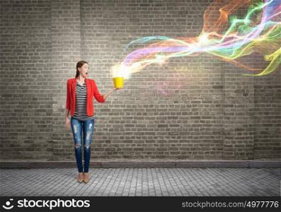 She is versatile and creative. Young woman in casual holding yellow bucket and colorful light coming out