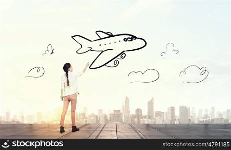 She likes traveling. Young girl standing with back and drawing airplane in sky