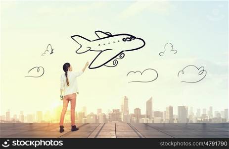 She likes traveling. Young girl standing with back and drawing airplane in sky