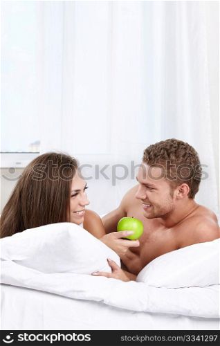 She offers the man a green apple in the bedroom