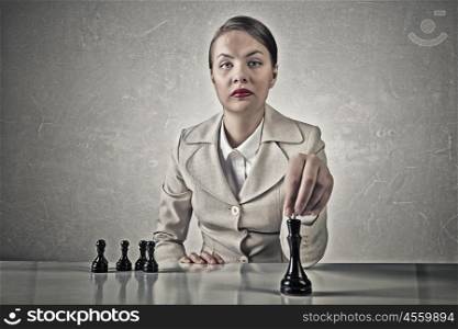She plays her strategy. Young pretty businesswoman sitting at table and playing chess