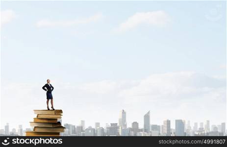 She reached the top. Confident businesswoman standing on pile of books