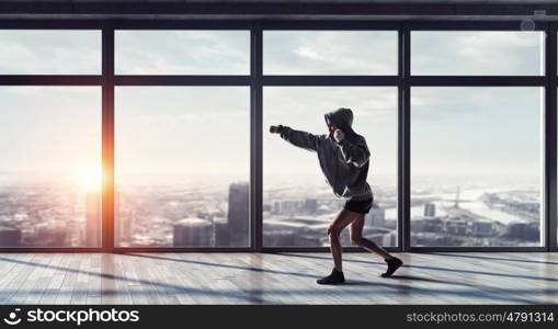 She will be a champ. Young boxer woman exercising in empty room in lights of sunrise. Mixed media