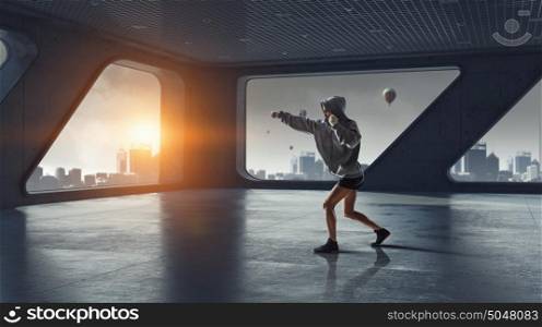 She will be a champ. Young boxer woman exercising in empty room in lights of sunrise. Mixed media