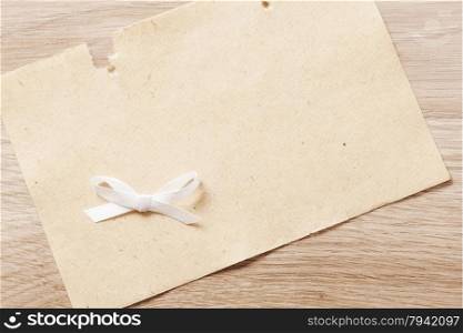 sheet of paper with white bow on a wooden background