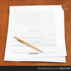 sheets of sales contract and golden pen on wooden table