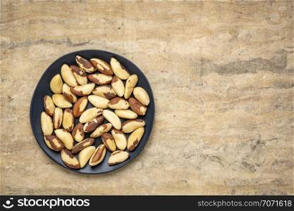 shelled Brazilian nuts on a black plate against textured handmade paper background with a copy space