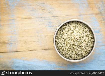shelled hemp seeds (hearts) in a ceramic bowl against rustic, grunge wood with a copy space, top view