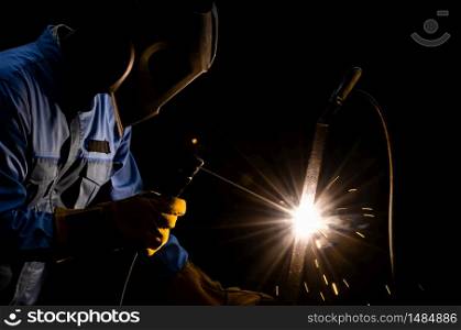 Shielded metal arc welding with sparks. A man welder in blue uniform with welding helmet and yellow leather gloves. Industrial working with personnel protective equipment concept.
