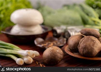 Shiitake mushrooms are on a plate on a wooden grill with spring onions and buns. Selective focus.