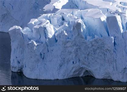 Shimmering blue high glacier tongue bends shortly before calving into cold sea water