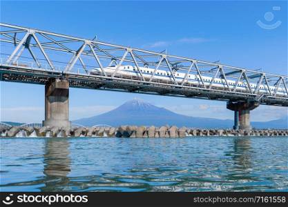 Shinkansen train. Fast bullet train, driving and passing Mountain Fuji near Tokyo railway station with steel bridge over Fuji river, Shizuoka, Japan
