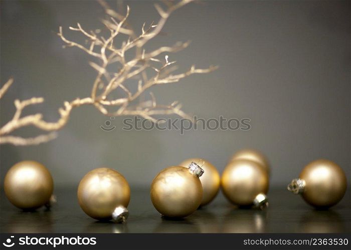 shiny and matt gold colored christmas tree toys and branch of a tree on a gray background. christmas tree ball shaped toys