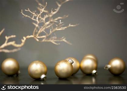 shiny and matt gold colored christmas tree toys and branch of a tree on a gray background. christmas tree ball shaped toys