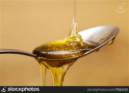 Shiny golden honey dripping off of a silver spoon with a wooden brown background sweet. Shiny golden honey dripping off of a silver spoon with a wooden brown background