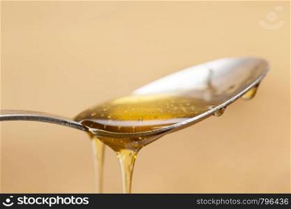 Shiny golden honey dripping off of a silver spoon with a wooden brown background sweet. Shiny golden honey dripping off of a silver spoon with a wooden brown background