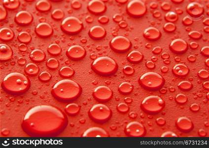 Shiny water drops sprayed on textured red surface.