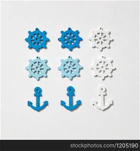 Ship anchors and wheel different colors pattern on a light grey background with hard shadows, copy space. Flat lay. Marine pattern from anchors and wheels.