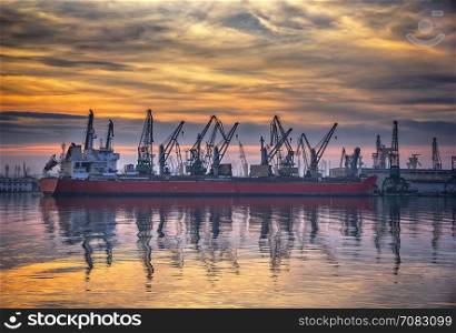 Ship and cranes in port at sunset. Cargo ship terminal at twilight scene.