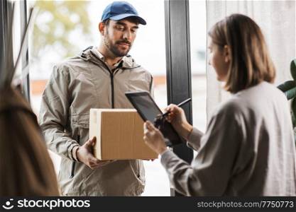 shipping, mail service and people concept - delivery man with parcel box and customer signing digital form in tablet pc computer at home. delivery man with box and woman signs digital form