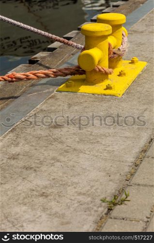 Shipping objects concept. Sailing ropes tied around yellow marina pins. Outdoor shot on sunny day.. Sailing ropes tied around pins in sunlight