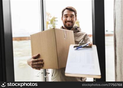 shipping, transportation and people concept - happy smiling delivery man with parcel box and clipboard at open door. smiling delivery man with parcel box at open door