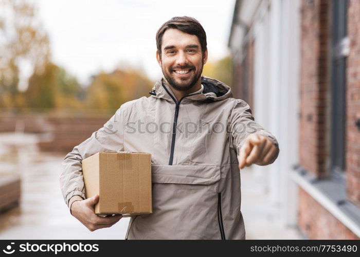 shipping, transportation and people concept - happy smiling delivery man with parcel box pointing finger to camera. delivery man with parcel box pointing to camera