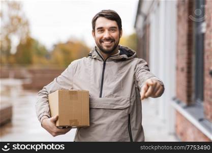 shipping, transportation and people concept - happy smiling delivery man with parcel box pointing finger to camera. delivery man with parcel box pointing to camera