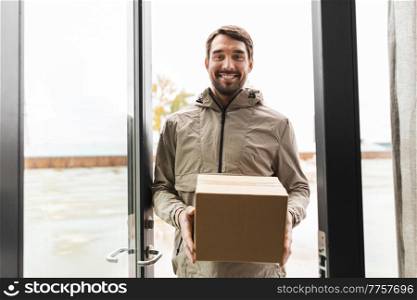 shipping, transportation and people concept - happy smiling delivery man with parcel box at open door. smiling delivery man with parcel box at open door
