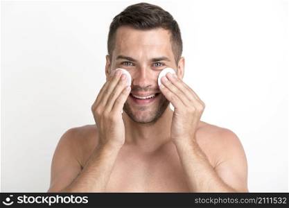 shirtless man cleaning his face with batting cotton pads white background looking camera