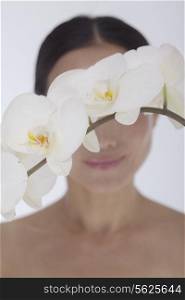 Shirtless smiling woman behind a bunch of beautiful white flowers, obscured face, studio shot