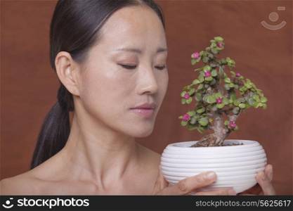 Shirtless woman holding and looking down at a small plant in a flower pot, studio shot