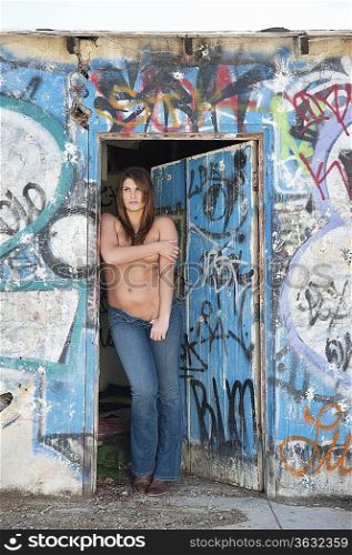 Shirtless woman in jeans standing at the entrance by graffiti wall and door
