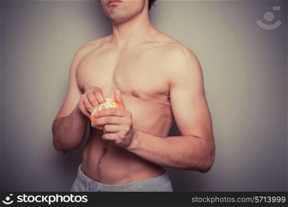 Shirtless young man peeling an orange