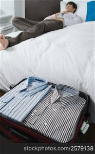 Shirts in a suitcase and a businessman sleeping on the bed