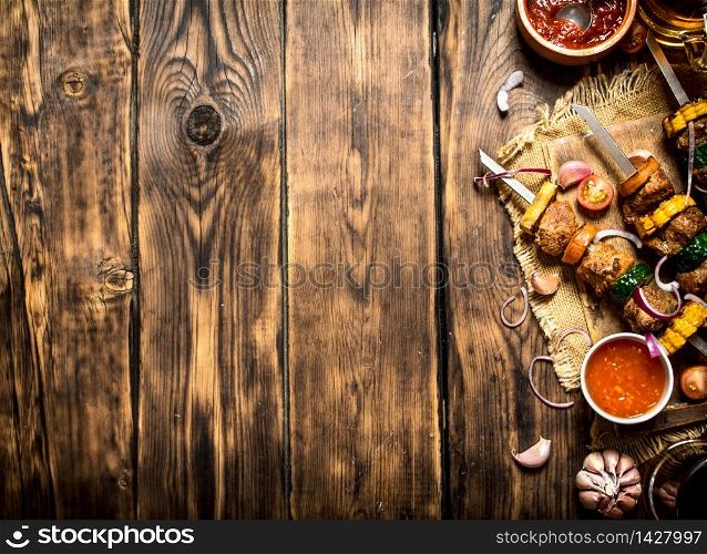Shish kebab of meat and vegetables with the sauce.On wooden background.. Shish kebab of meat and vegetables with the sauce.