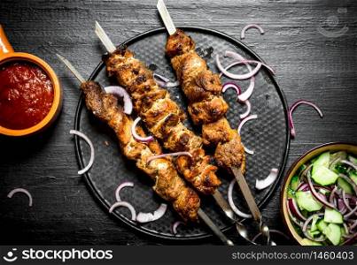 Shish kebab of pork and salad. On the black wooden table.. Shish kebab of pork and salad.