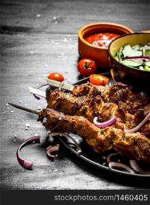 Shish kebab of pork and salad. On the black wooden table.. Shish kebab of pork and salad.