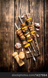 Shish kebab of pork and vegetables on skewers. On wooden background.. Shish kebab of pork and vegetables on skewers.