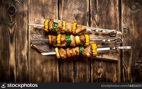 Shish kebab of pork and vegetables on skewers. On wooden background.. Shish kebab of pork and vegetables on skewers.