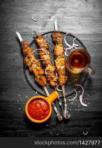 Shish kebab on skewers with beer and tomato sauce. On the black wooden table. Shish kebab on skewers with beer and tomato sauce.