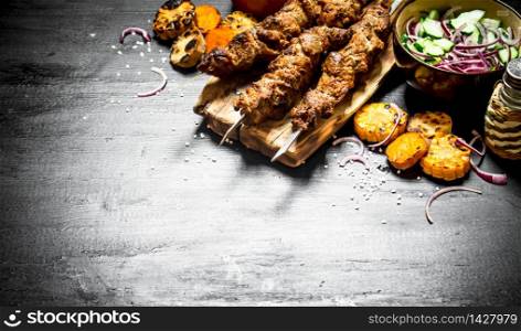 Shish kebab on skewers with grilled vegetables and fresh salad. On the black wooden table.. Shish kebab on skewers with grilled vegetables and fresh salad.