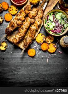 Shish kebab on skewers with grilled vegetables and fresh salad. On the black wooden table.. Shish kebab on skewers with grilled vegetables and fresh salad.