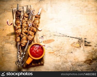 Shish kebab on skewers with tomato sauce on the Board. On a wooden table.. Shish kebab on skewers