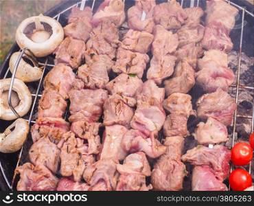 Shish kebab prepared over a black round shaped charcoal barbecue outdoors