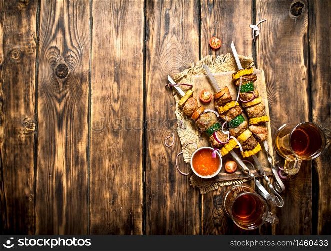 Shish kebab with beer and hot sauce. On wooden background. Shish kebab with beer and hot sauce.