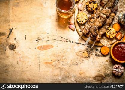 Shish kebab with roasted vegetables and beer. On a wooden table.. Shish kebab with roasted vegetables and beer.