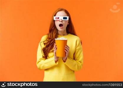 Shocked and tensed redhead woman seeing intense fight on screen as watching movie at cinema, wear 3d glasses, holding popcron, frowning and gasping concerned, orange background.. Shocked and tensed redhead woman seeing intense fight on screen as watching movie at cinema, wear 3d glasses, holding popcron, frowning and gasping concerned, orange background