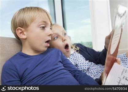 Shocked brother and sister reading storybook at home